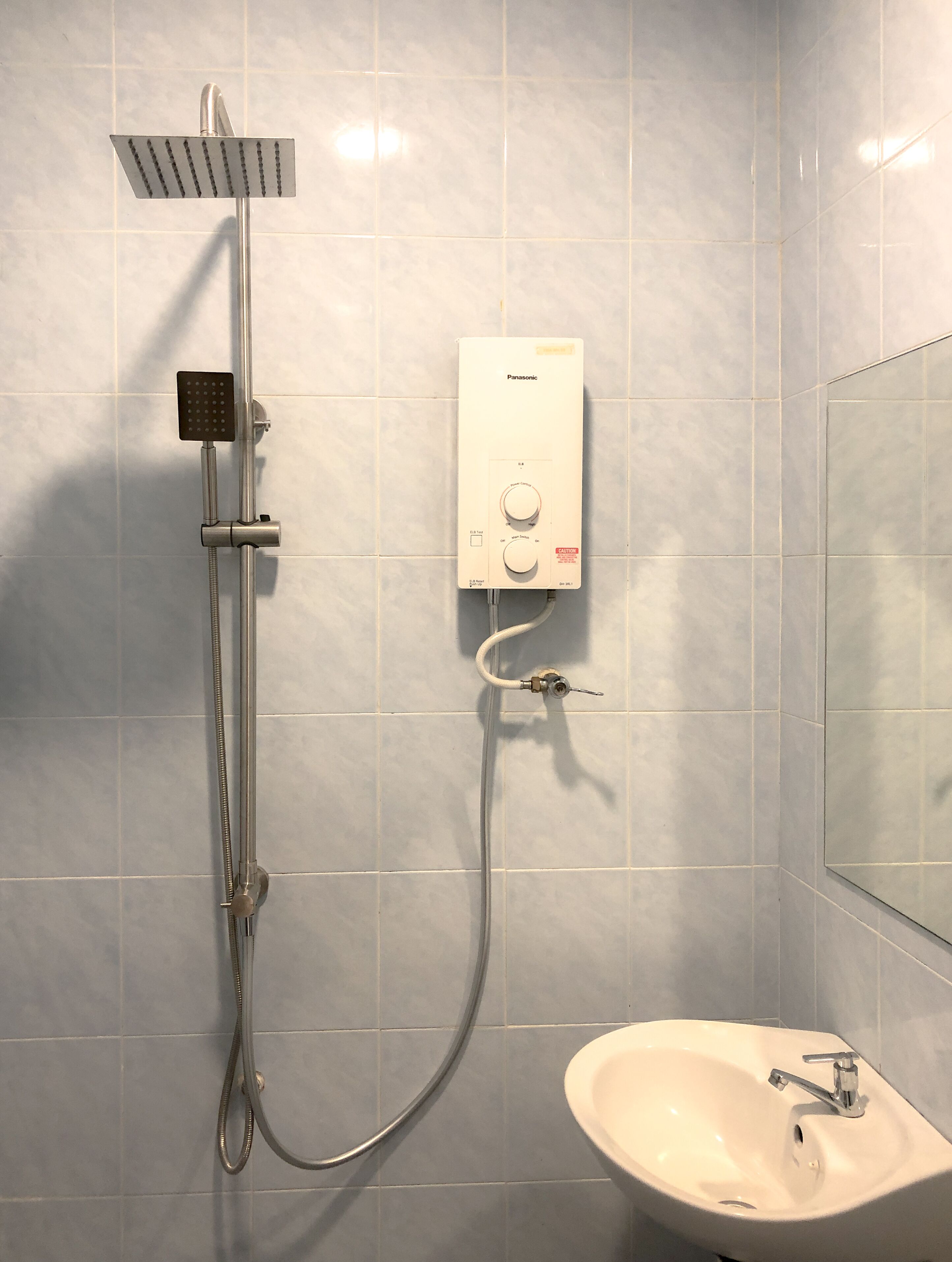 Een badkamer met een douche, een wastafel en een bedieningspaneel aan de muur.