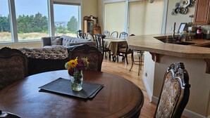 A dining area with a round wooden table, a vase of flowers, and a view of the outdoors through large windows. - 3 Master Suites, Spa, Pool table, Game room, views (Tillamook)