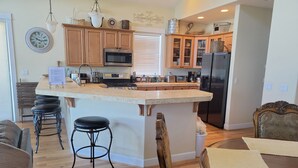 A modern kitchen with wooden cabinets, a central island, bar stools, and a dining area with a wooden table and chairs. - 3 Master Suites, Spa, Pool table, Game room, views (Tillamook)