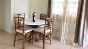Een eetgedeelte met een ronde tafel, vier rieten stoelen, een fles wijn en twee wijnglazen.