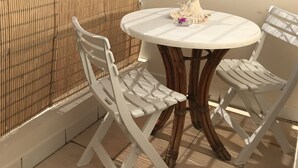 Een balkon met een ronde tafel en twee witte stoelen, een bamboe hek en uitzicht op een groene heuvel.