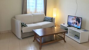 Een woonkamer met een bank, een salontafel, een tv op een dressoir en een lamp.