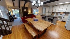 Een ruime woonkamer met een houten eettafel, een rode bank en een stenen open haard.