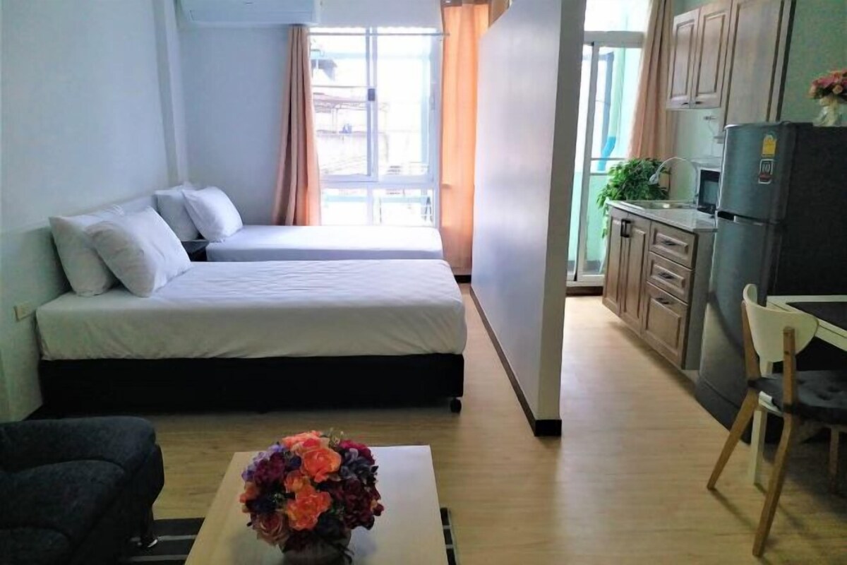 Habitación de hotel compacta con dos camas, una kitchenette pequeña, zona de comedor y ventana con cortinas.