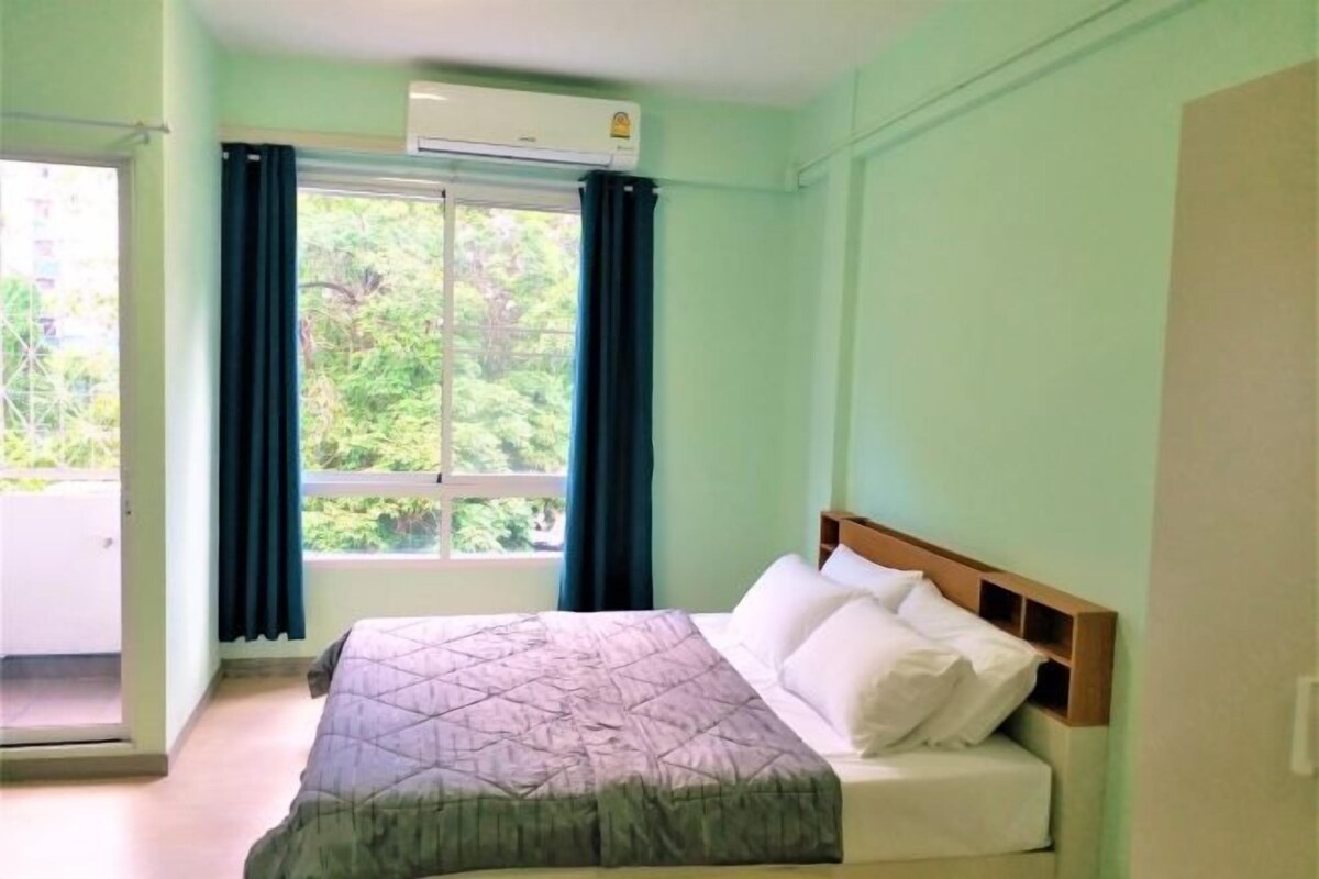 Un dormitorio con cama, ventana con cortinas, aire acondicionado y vistas a zonas verdes.