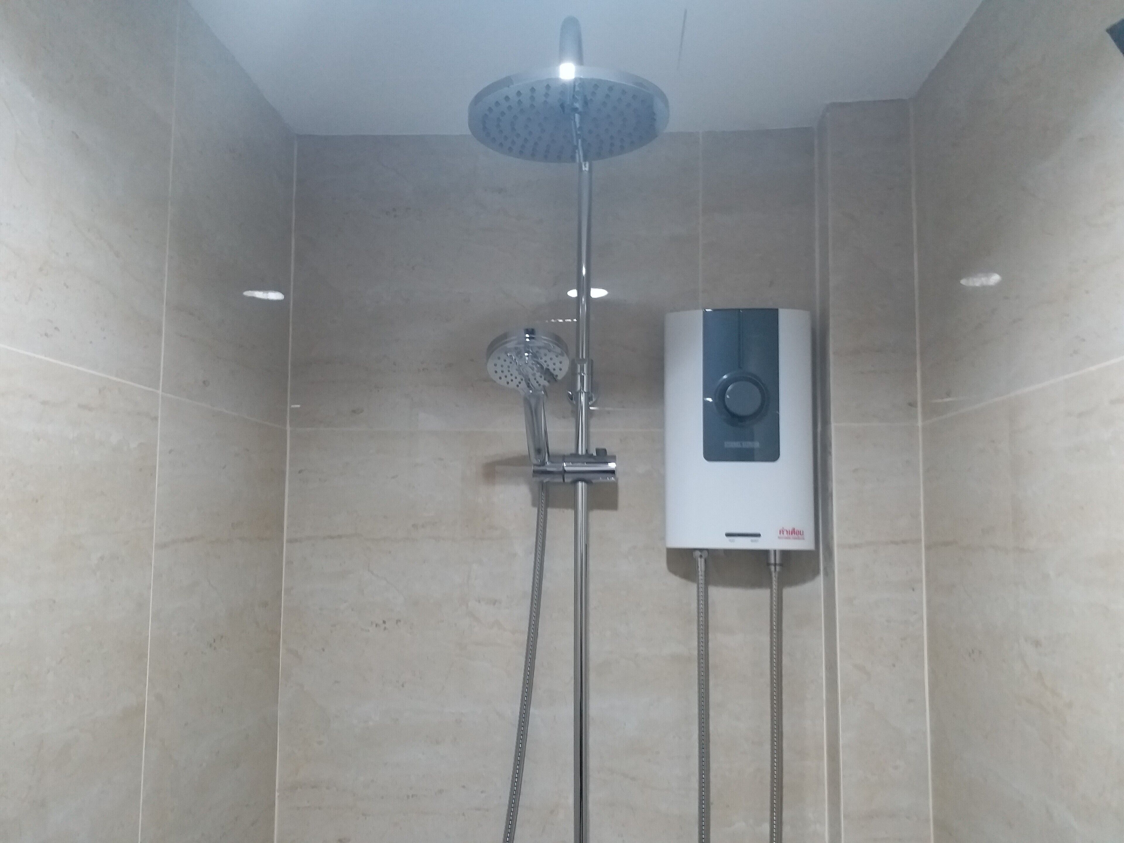 A shower area with a handheld showerhead and a wall-mounted heater.