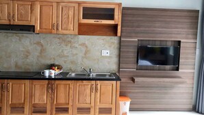 A kitchen with wooden cabinets, a stainless steel sink, a built-in oven, and a wall-mounted TV. - Nhat Thu Hotel & Apartment (Ho Chi Minh City)