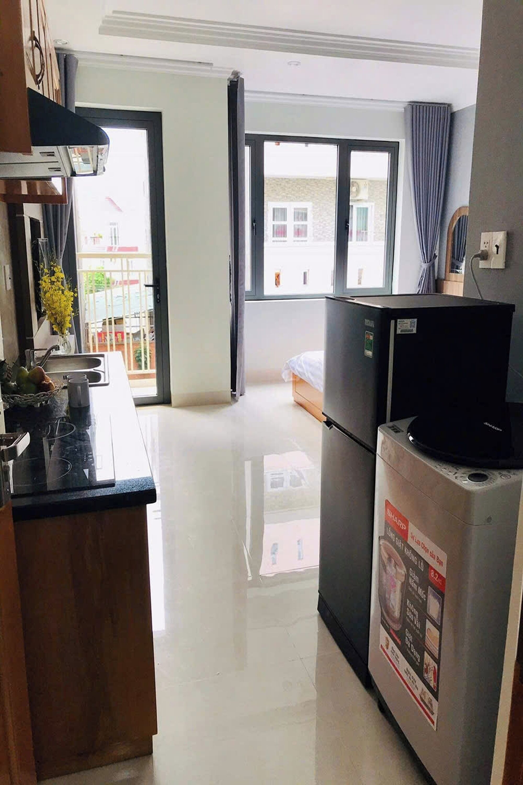 Una cocina compacta con refrigerador, microondas y lavamanos. Hay una ventana con vista a edificios.