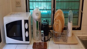 A kitchen with a white microwave, a coffee maker, a toaster, and a dish rack with plates. - Sirin Bungalow (Choeng Thale)