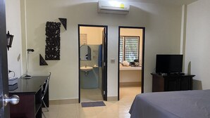 A hotel room with a bed, a desk, a chair, a television, and a bathroom visible through an open door. - Sirin Bungalow (Choeng Thale)