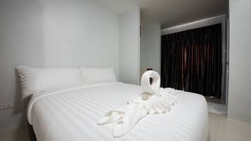 A neatly made bed with a white comforter and pillows, a robe draped over the side, and a window with dark curtains.