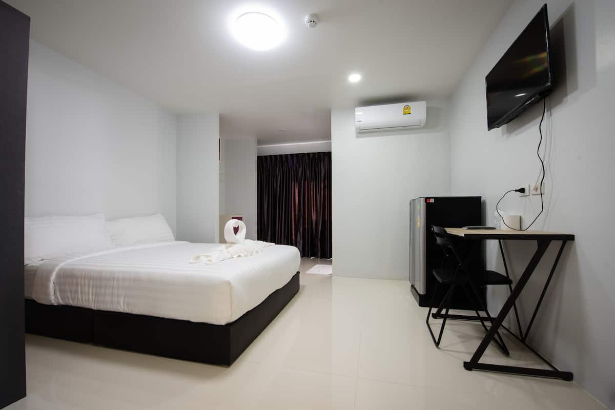 A hotel room with a bed, a desk, a chair, a TV, and an air conditioning unit.