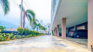 A covered parking area with cars parked under a structure, surrounded by greenery and palm trees. - Tyler Cherngtalay (Choeng Thale)