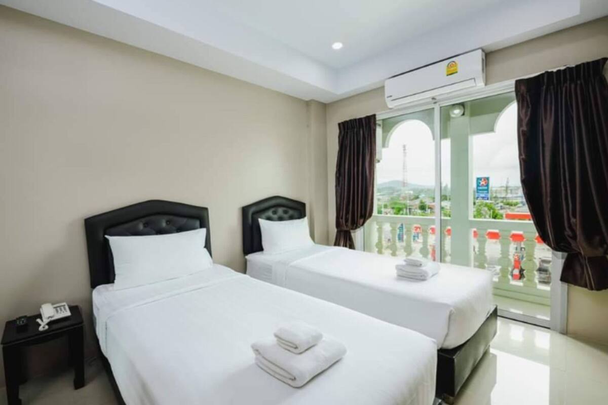 A hotel room with two beds, a small bedside table with a phone, and a balcony with curtains.