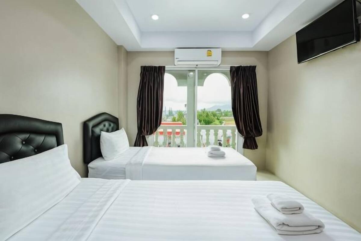 A hotel room with two beds, a TV, an air conditioning unit, and a balcony with curtains.