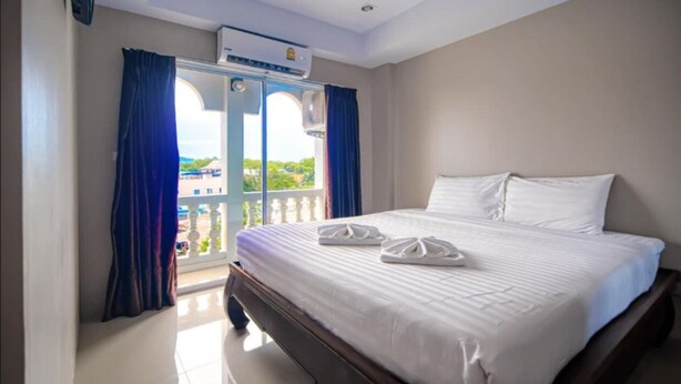 A hotel room with a large bed, a balcony with curtains, and an air conditioning unit. - Tyler Cherngtalay (Choeng Thale)