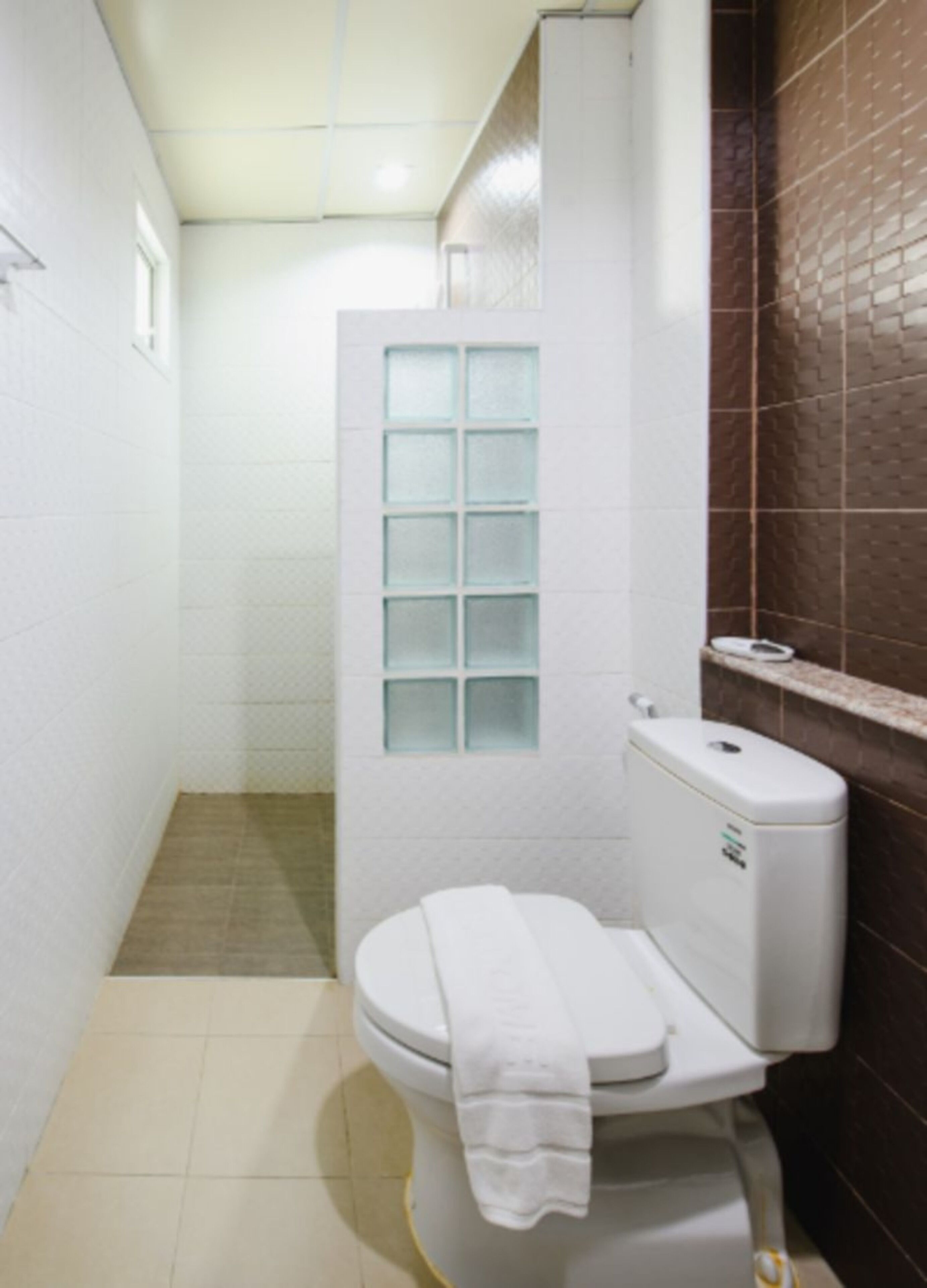 Un baño pequeño y funcional con inodoro blanco, ducha con mampara de vidrio y pared de azulejos marrones.
