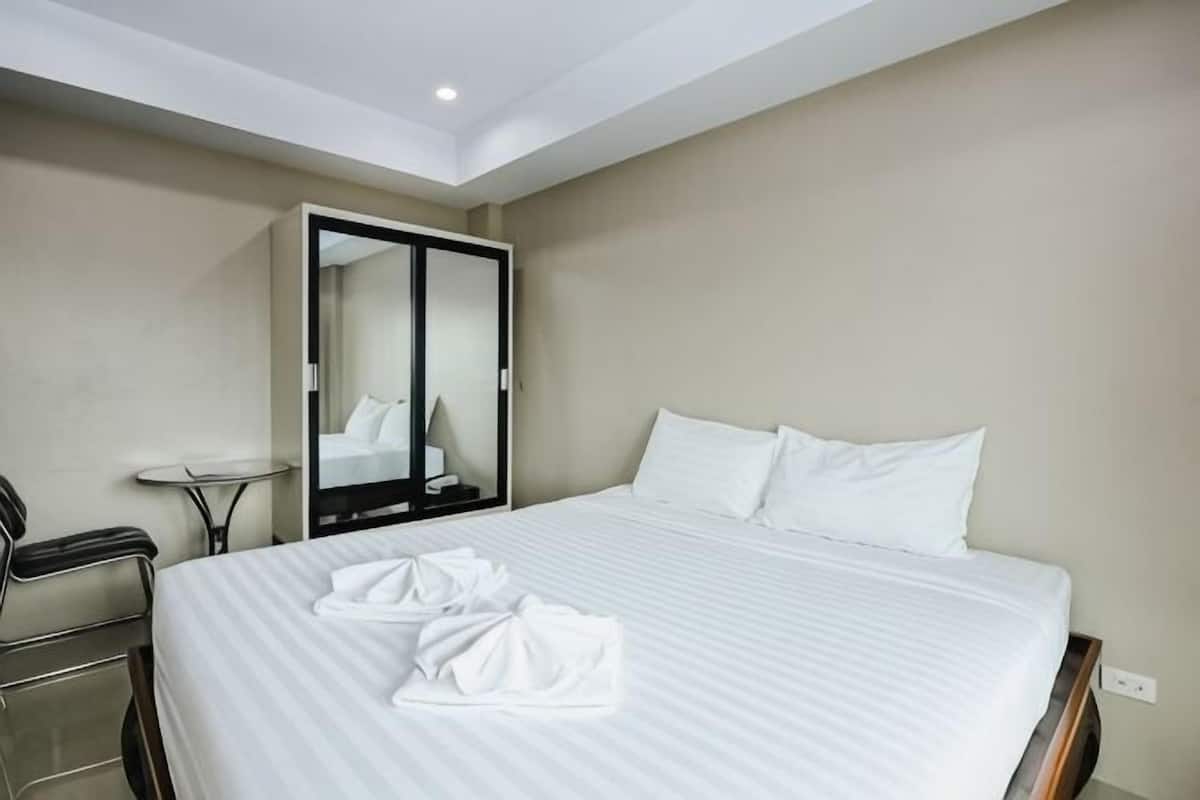 A hotel room with a bed, a desk, a chair, a mirror, and a wardrobe.
