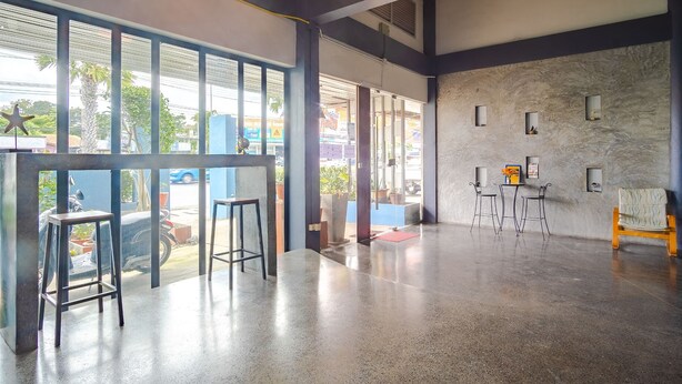A spacious lobby with a polished concrete floor, large windows, and a seating area with chairs and a small table. - Tyler Banpon (Si Sunthon)