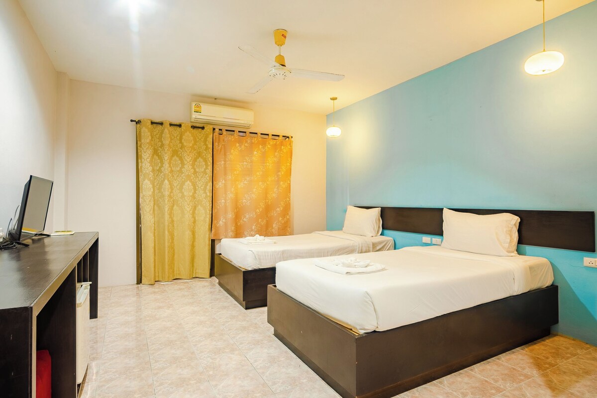 A hotel room with two beds, a desk, a ceiling fan, and a light fixture.