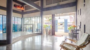 A spacious lobby with a polished floor, large windows, and a seating area with a chair. - Tyler Banpon (Si Sunthon)