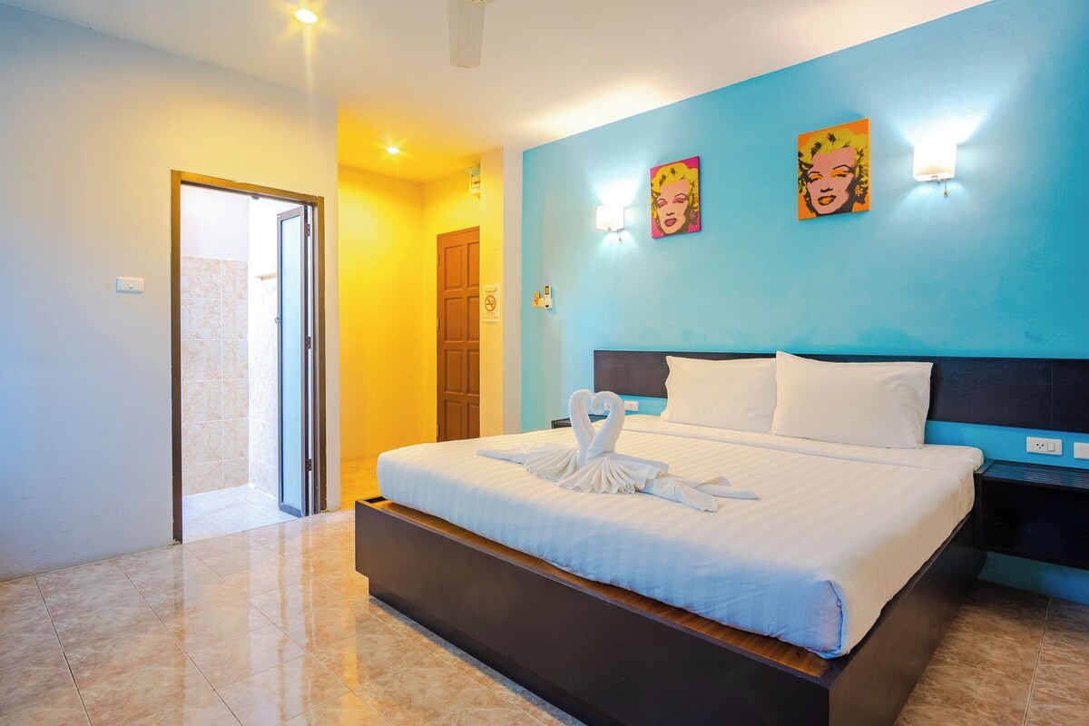 A hotel room with a large bed, a blue accent wall, and two wall-mounted lights.