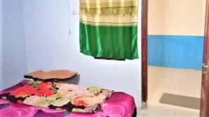 A small room with a bed covered in a floral bedspread, a green and gold curtain, and a blue wall. - Ijen Miner Guest House (Banyuwangi)