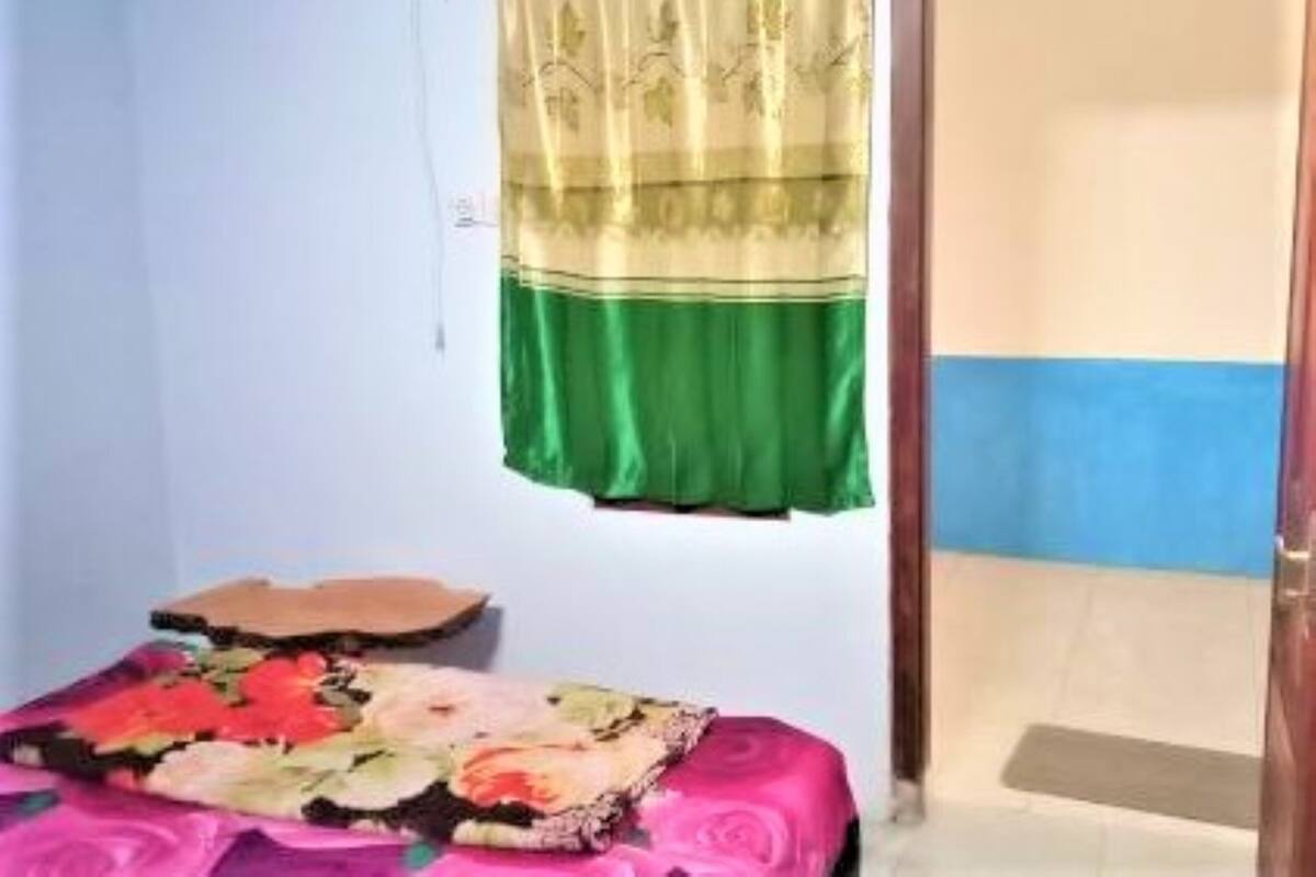 A small room with a bed covered in a floral bedspread, a green and gold curtain, and a blue wall.