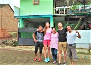 A group of people standing in front of a house with a green exterior and a balcony with potted plants. - Ijen Miner Guest House (Banyuwangi)