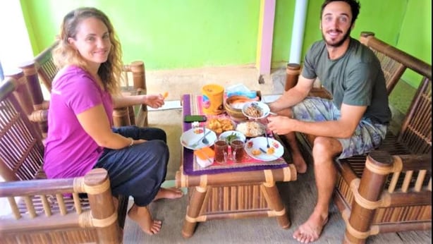 Two people seated on wooden chairs at a small table with various food items. - Ijen Miner Guest House (Banyuwangi)