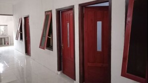 A hallway with multiple red doors and windows, white walls, and a tiled floor. - Ijen Miner Guest House (Banyuwangi)