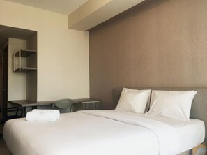A hotel room with a bed, a desk, and a chair. - Galeri Ciumbuleuit 3 by Nu Apartment (Bandung)