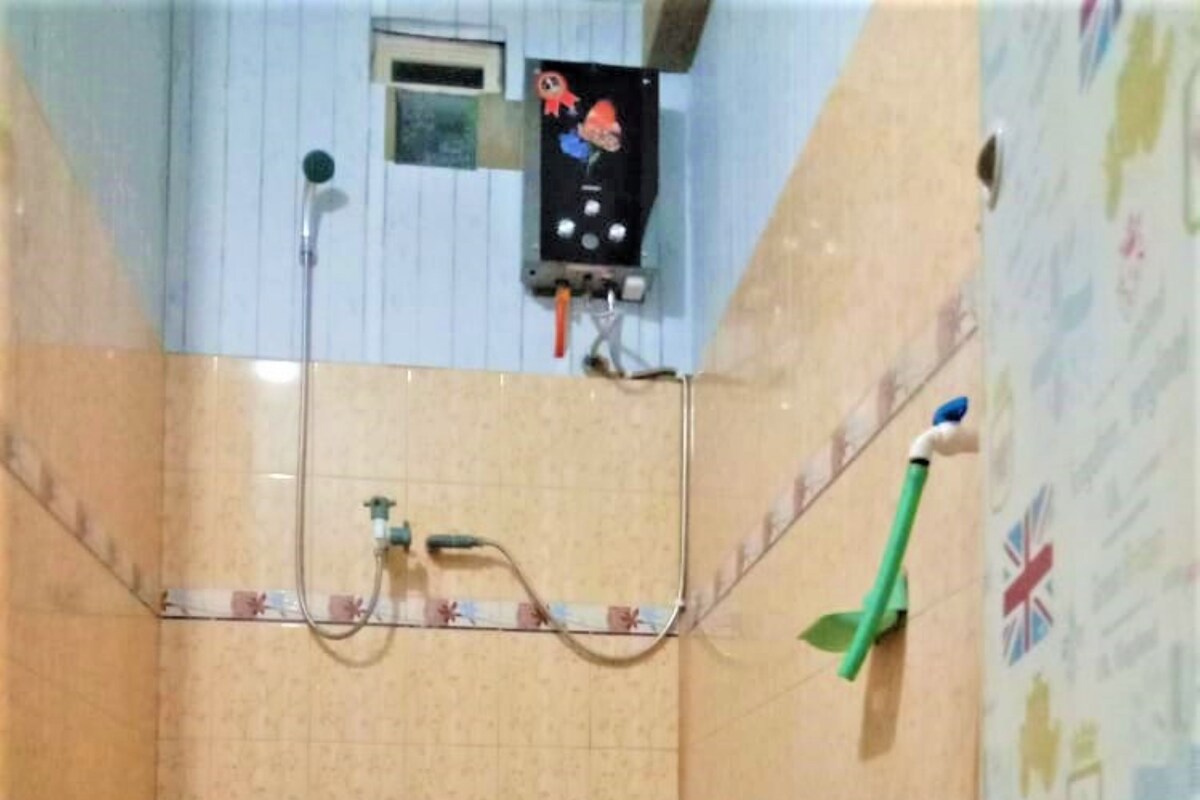 A bathroom with a shower, a toilet, and a sink. There is a window above the shower and a wall with a floral pattern.