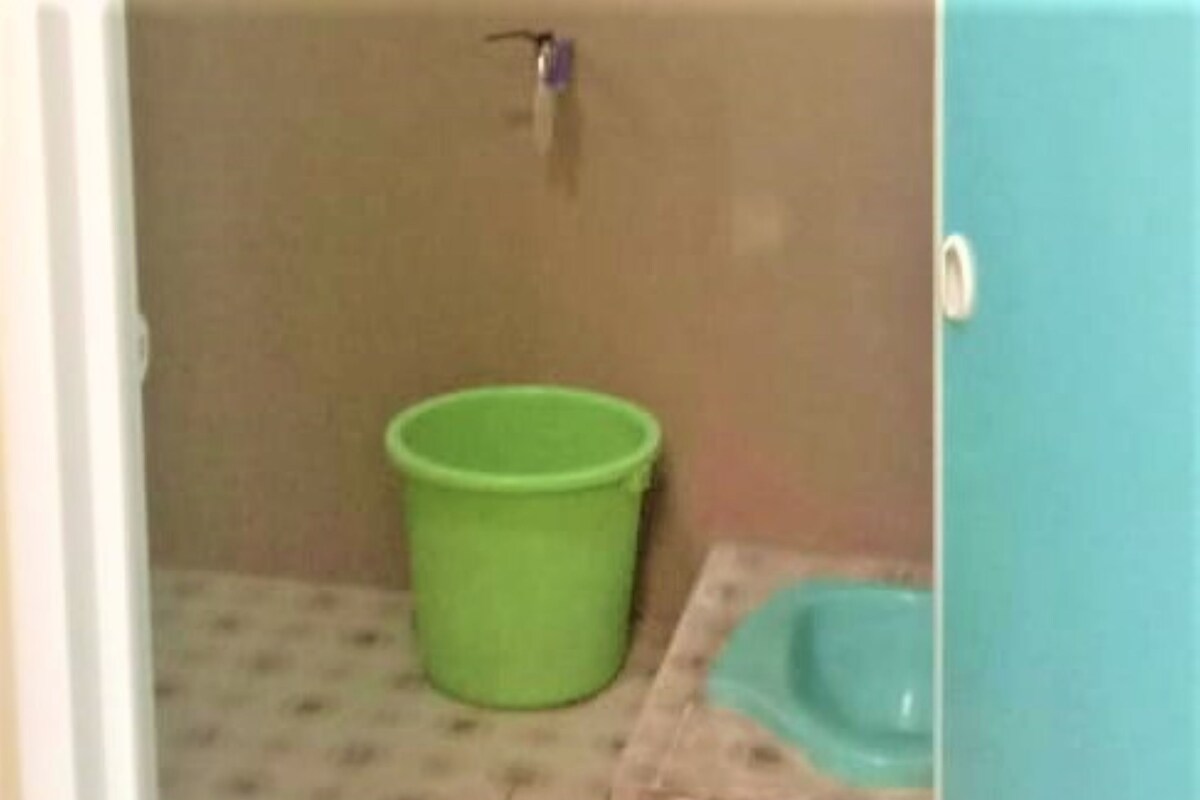 A bathroom with a green bucket, a blue sink, and a wall-mounted faucet.