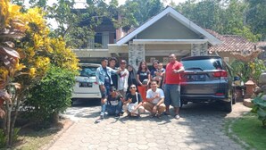 Un grupo de personas posando frente a una casa con un coche estacionado cerca.