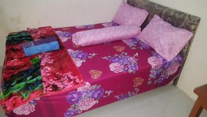 Un lit avec une couvre-lit à motifs floraux et deux oreillers, une couverture colorée et un oreiller bleu sur le côté gauche.