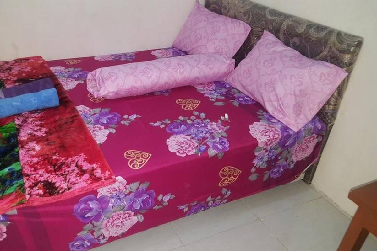 Un lit avec une couvre-lit à motifs floraux et deux oreillers, une couverture colorée et un oreiller bleu sur le côté gauche.