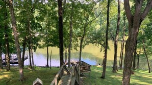 A wooden deck leading to a small wooden structure by a lake surrounded by trees. - Beautiful Waterfront, w/ Dock, Firepit, Hot tub (Cadiz)