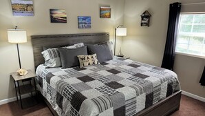 A bedroom with a large bed, two bedside tables, a headboard, and four wall-mounted pictures.