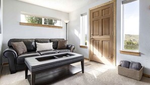 Una sala de estar con un sofá de cuero negro, una mesa de centro oscura y una puerta de madera.
