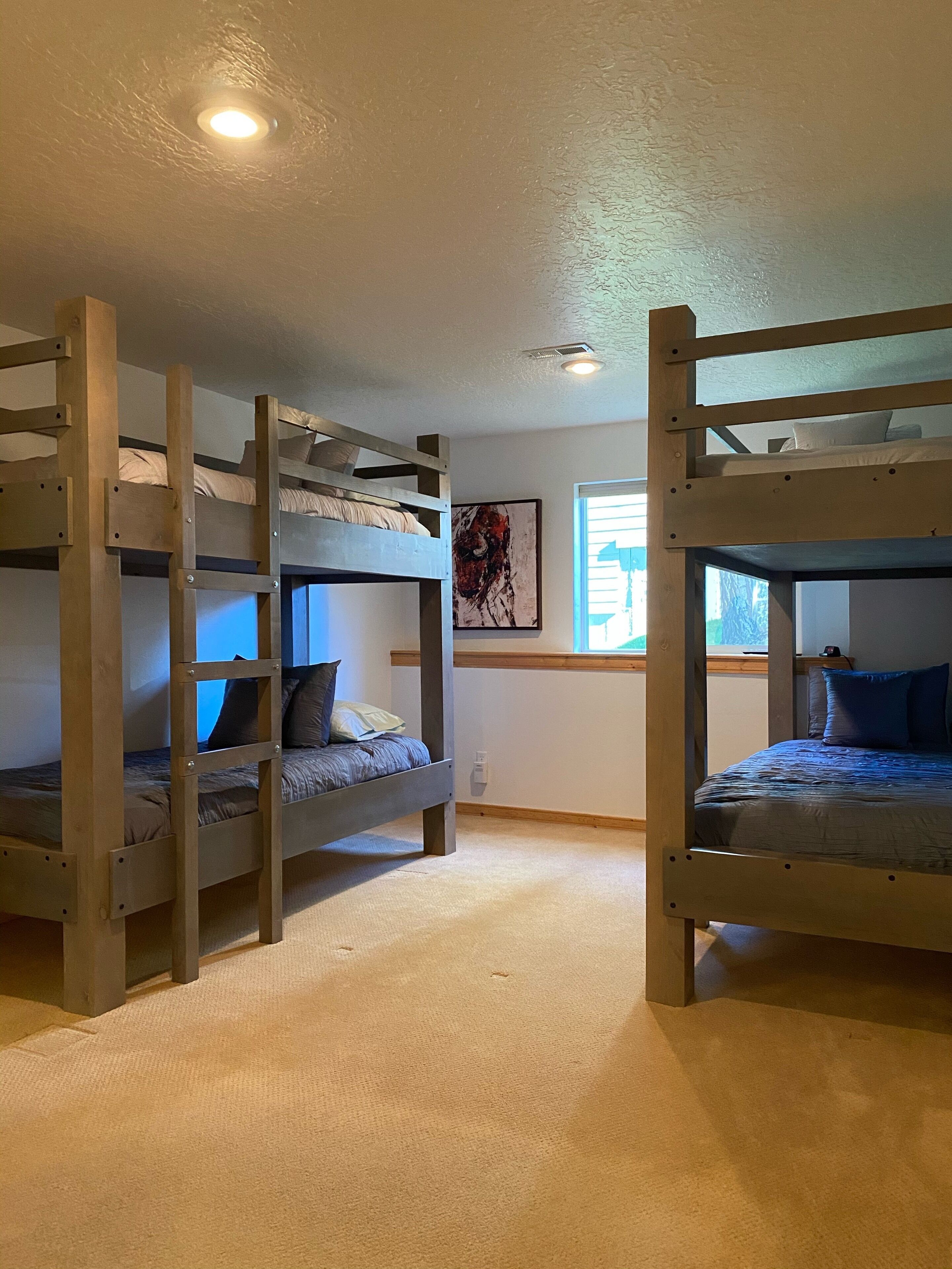 A room with three bunk beds arranged in a row, a ceiling light, and a window with blinds.