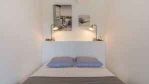 Camera da letto ordinata con un letto, due cuscini, due lampade a parete e due quadri appesi sopra il letto.