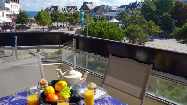 Un balcone con un tavolo apparecchiato per la colazione, con vista su una cittadina con edifici e alberi.