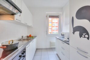 Cozinha moderna com armários brancos, fogão e janela com vista para edifícios.