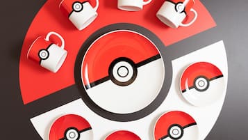 A circular arrangement of tableware with a Poké Ball design, including plates, bowls, and cups.