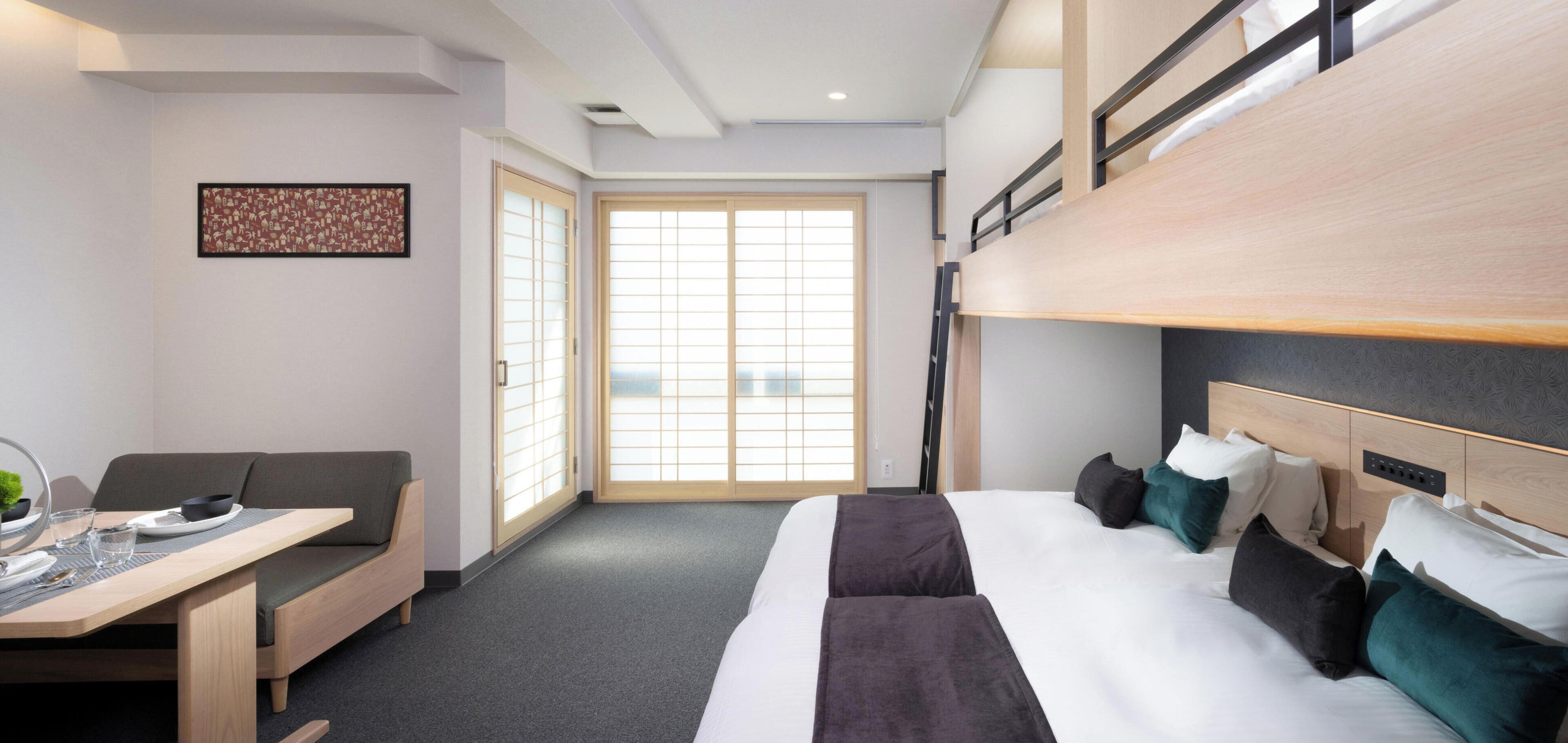 A hotel room with a bunk bed, a desk with a chair, a sofa, and a large window with a view.