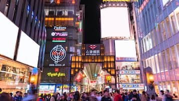 A busy urban street at night with illuminated signs and billboards, including a prominent 'WEGO' sign and a 'J'adoré' dining establishment.
