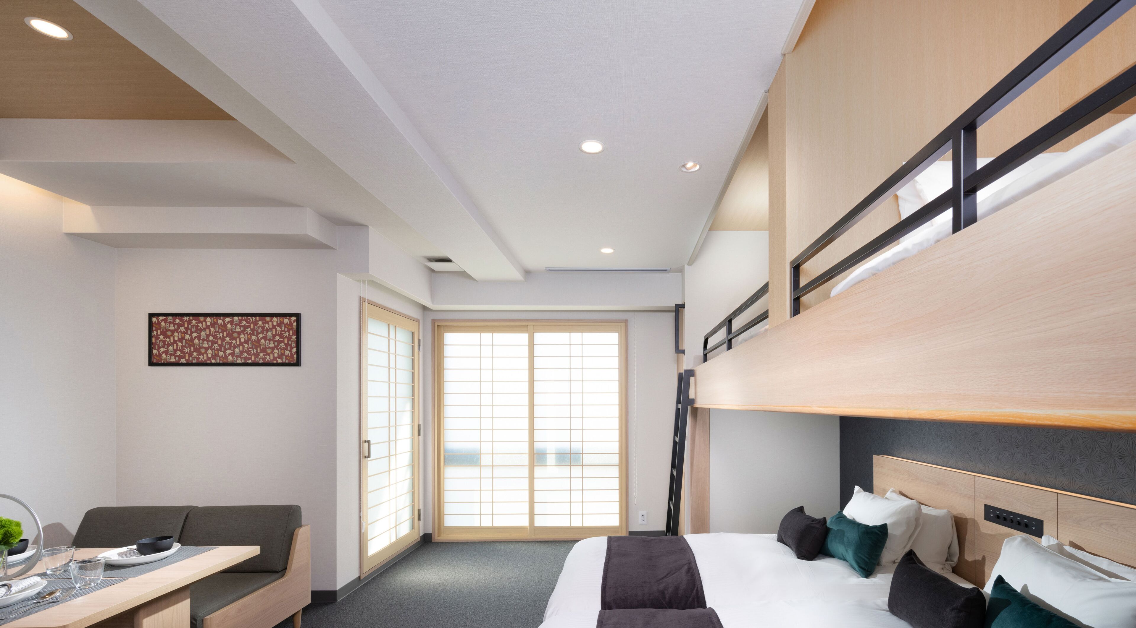 A modern hotel room with a bunk bed, a dining area with a table and chairs, and a large sliding glass door leading to a balcony.