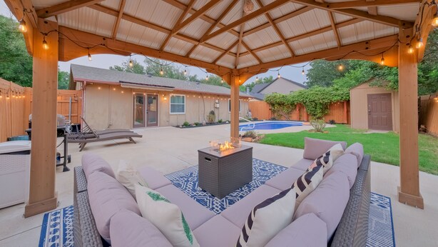 Un patio cubierto con una fogata, mobiliario exterior e iluminado con luces colgantes.