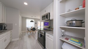 Una cocina moderna con armarios blancos, una estufa de acero inoxidable y un microondas. Se observa un comedor con una mesa y sillas al fondo.